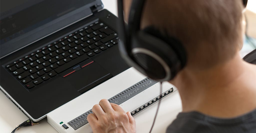 Image of a person using a braille keyboard with headphones.