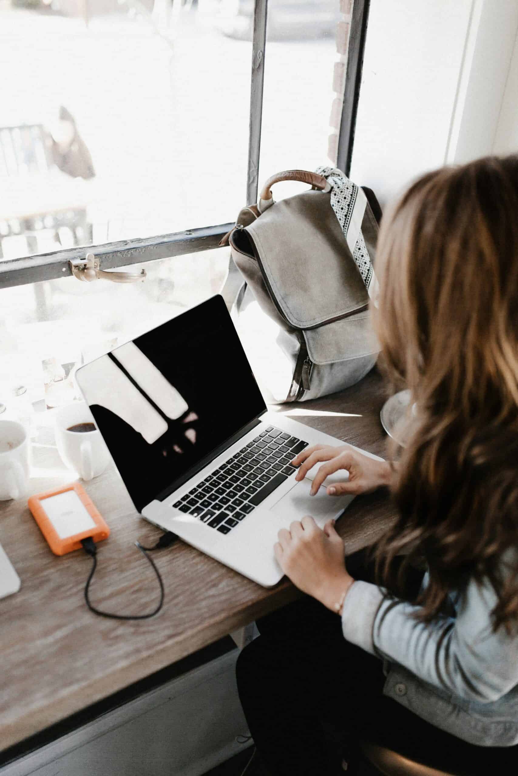 A woman at a coffee shop is working on her Mac laptop.